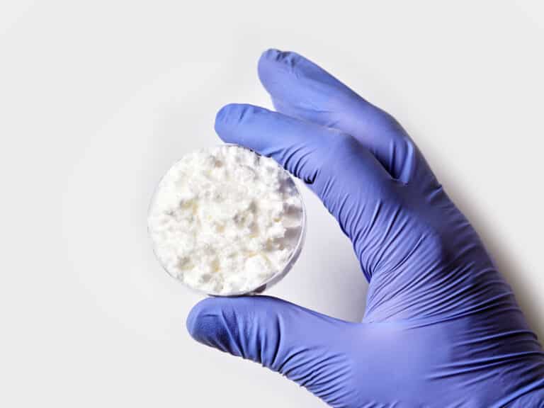 lab technician wearing purple glove holds a dish of bulk cbd isolate